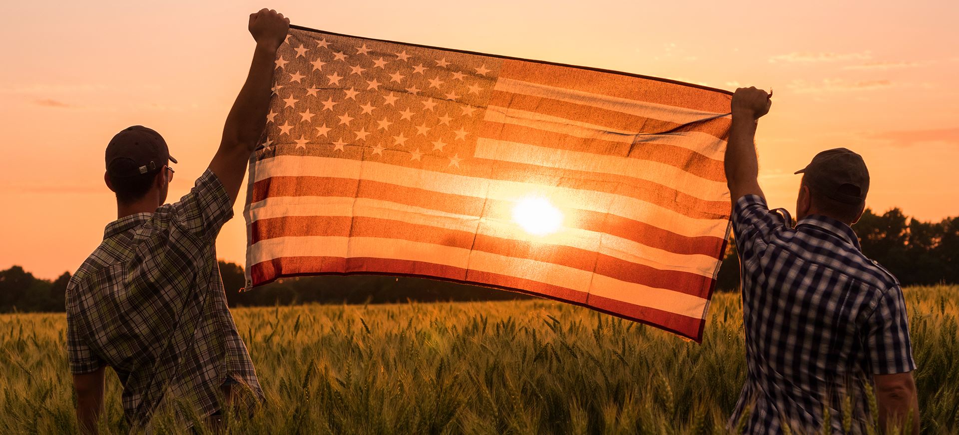 two men holding American flag during sunset